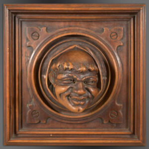 Trompe L'oeil carved in wood depicting a monk's head peeping out of a circular architectural roundel set within a square panel.
