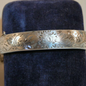 A hinged sterling silver bracelet with a narrow face engraved with scrolling foliates.