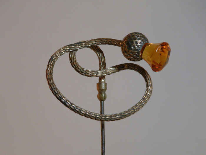 Hat Pin topped by a serpentine sterling silver thistle with an amber glass tip