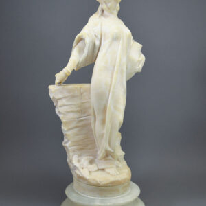A hand-carved alabaster sculpture of an edwardian woman holding an urn of water next to a well