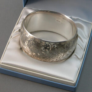 A sterling silver cuff form bracelet made by birks with heavily engraved decoration sitting within a Birks blue box.