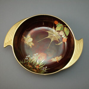 a round dish with spiral handles in the rouge royale colourway decorated with Spider Webb & Butterfly decoration