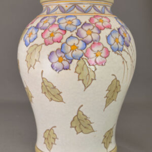 A large baluster vase is tubelined in pink, blue and purple flowers atop falling leaves on a faux-stoneware ground.