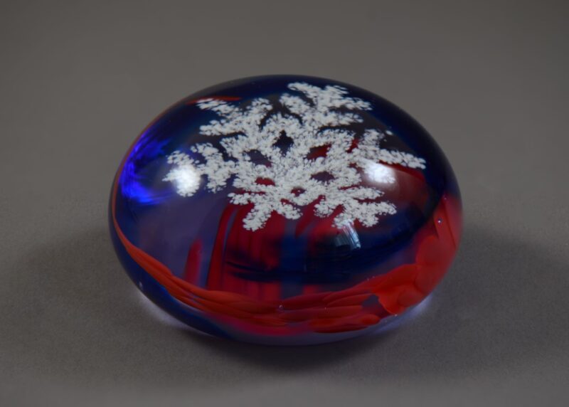 Caithness paperweight with a blue and red swirl around a suspended snowflake.