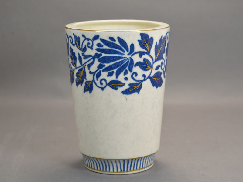 The cylindrical planter is tube-lined around the rim with an elaborate scrolling carnation pattern in blue with gilt highlights, the rim is also gilt, as is the slightly concave foot.
